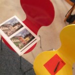 Auf Stühlen in verschiedenen Farben liegen Zettel zum Notieren für Ideen und inspirierende Fotomontagen der Häuser im Lollfuß mit bunten Fassaden.